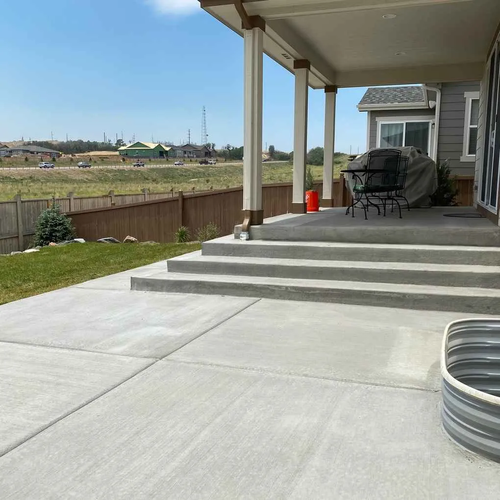 Broom-finish concrete patio with broad steps leading to a covered porch