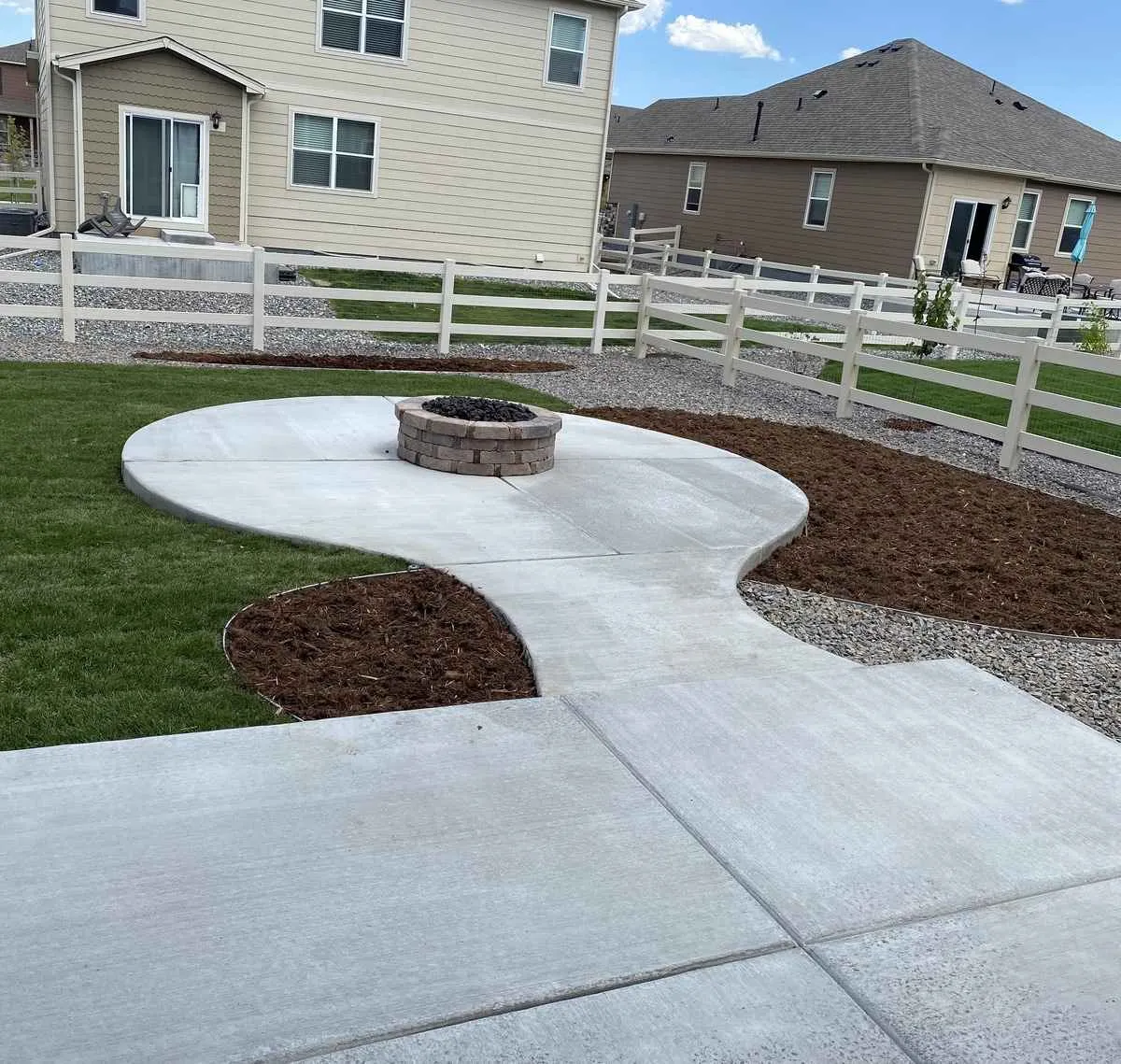 Round built-in masonry fire pit on a curved concrete pad connected by a walkway