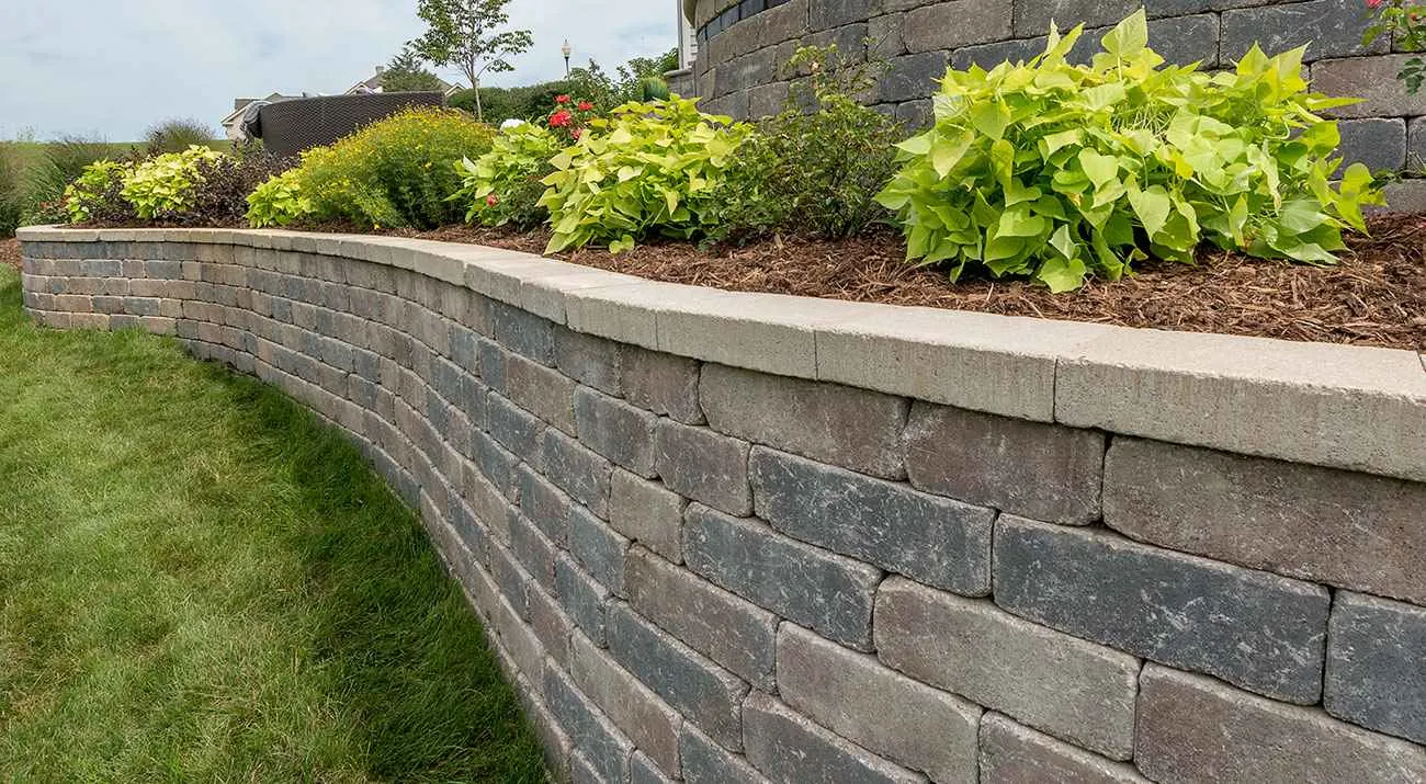 Curved segmental-block retaining wall supporting a planted bed beside a lawn