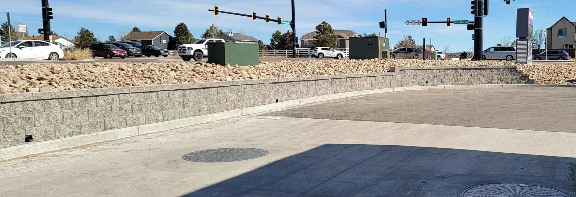 Long concrete-block retaining wall beside a paved access area and rock-covered slope
