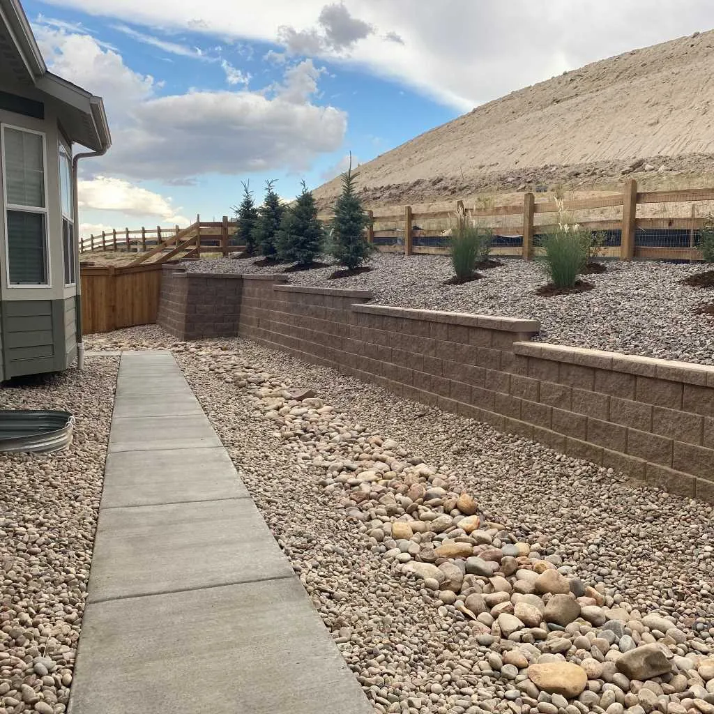 Block retaining wall beside a concrete walk and a rock drainage channel