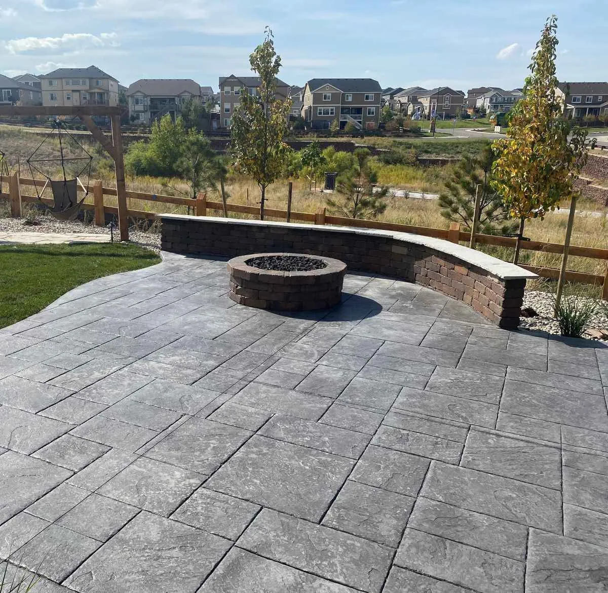 Stamped concrete patio with a fire-pit surround, curved seating wall, lawn, and planting