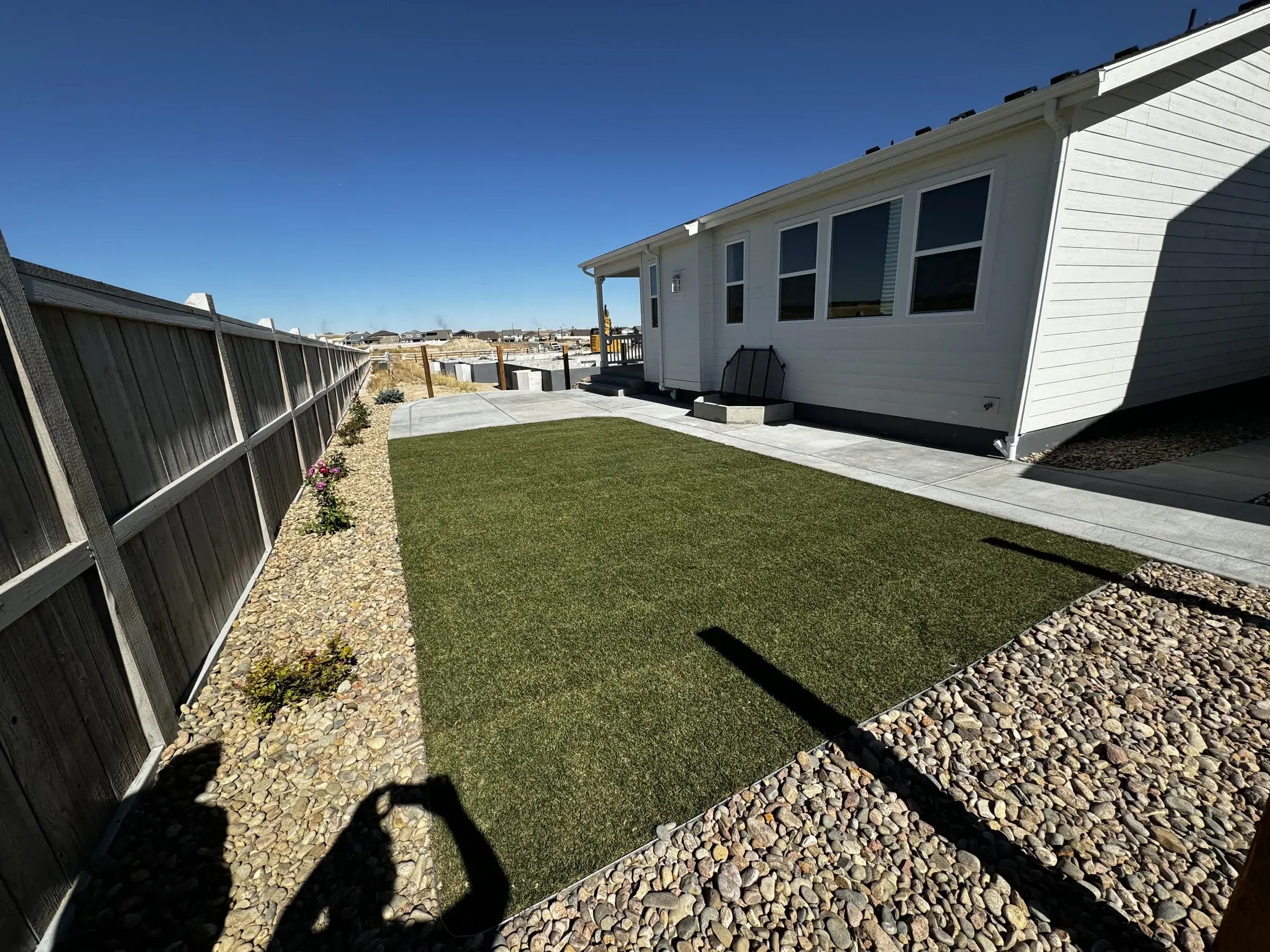 Backyard artificial turf lawn with a concrete patio and rock border along a wood fence in Parker
