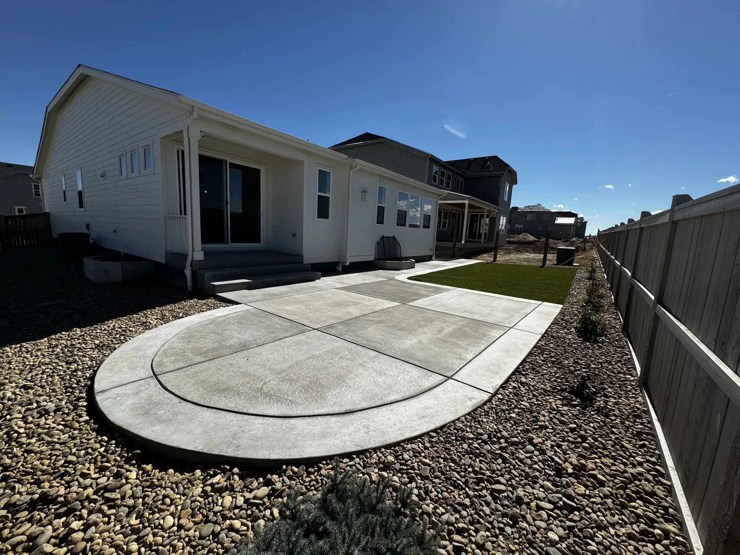 Rounded concrete patio with rock borders and an artificial turf accent area in Parker