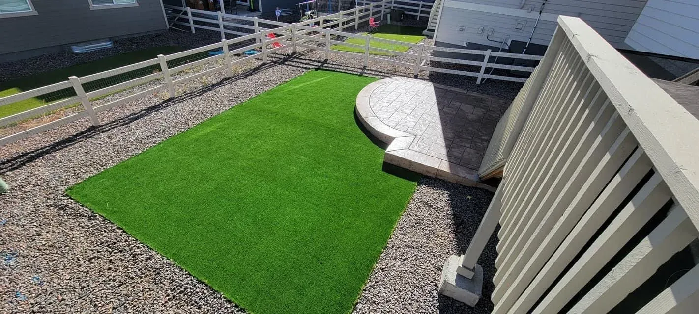 Backyard with artificial turf, a curved stamped concrete patio, and white vinyl fencing in Castle Rock
