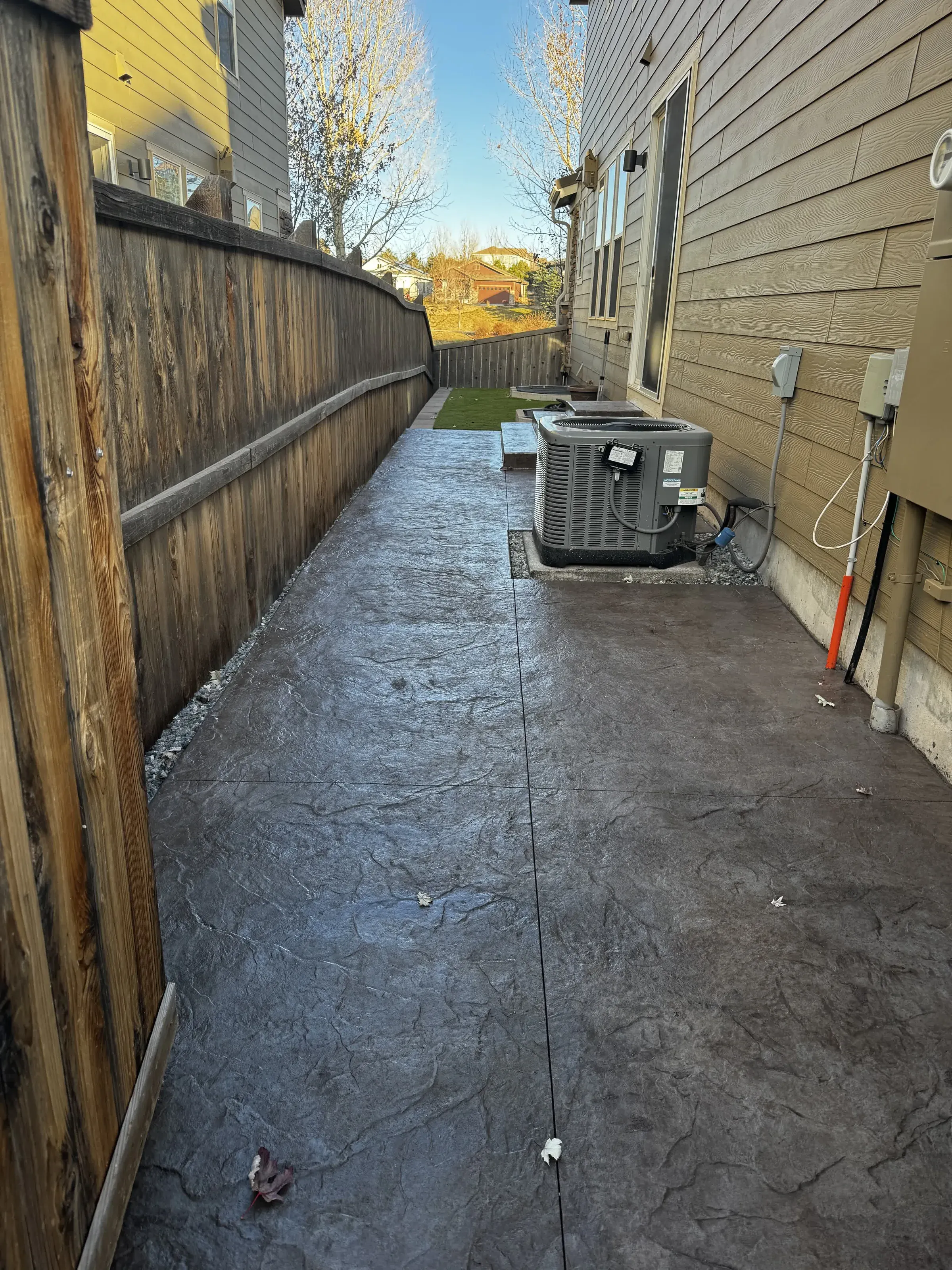 Stamped concrete side-yard walkway leading to a small backyard turf area in Parker