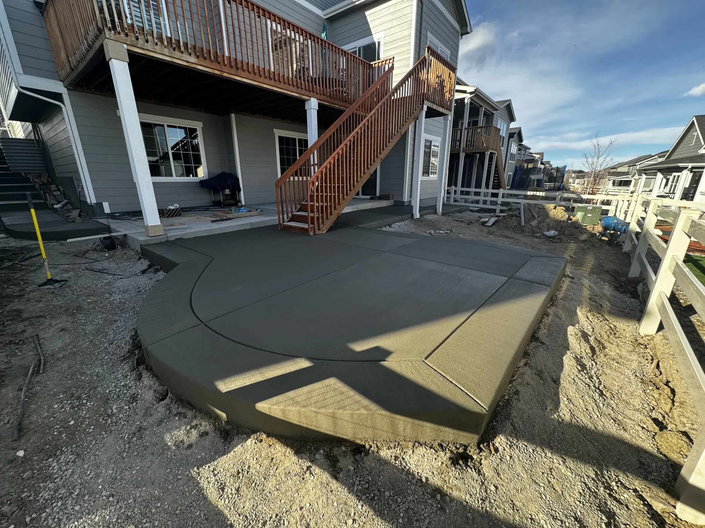 Freshly poured curved concrete patio beneath a two-story deck in Castle Rock