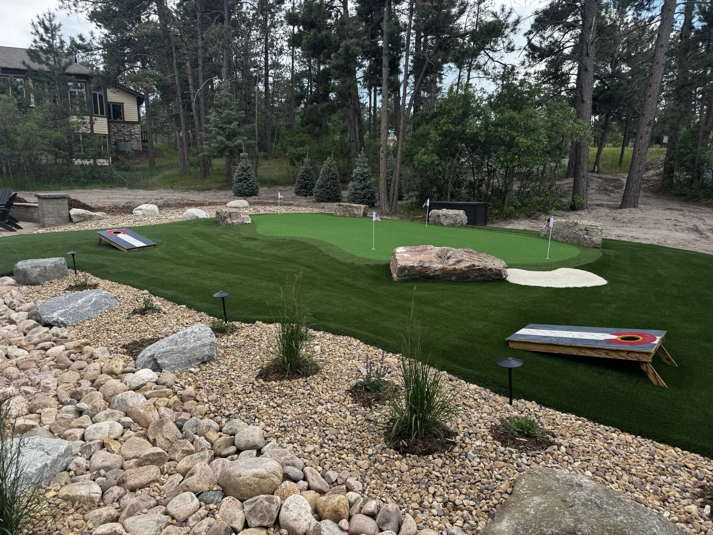 Backyard artificial turf putting green with boulder accents and cornhole boards in Larkspur