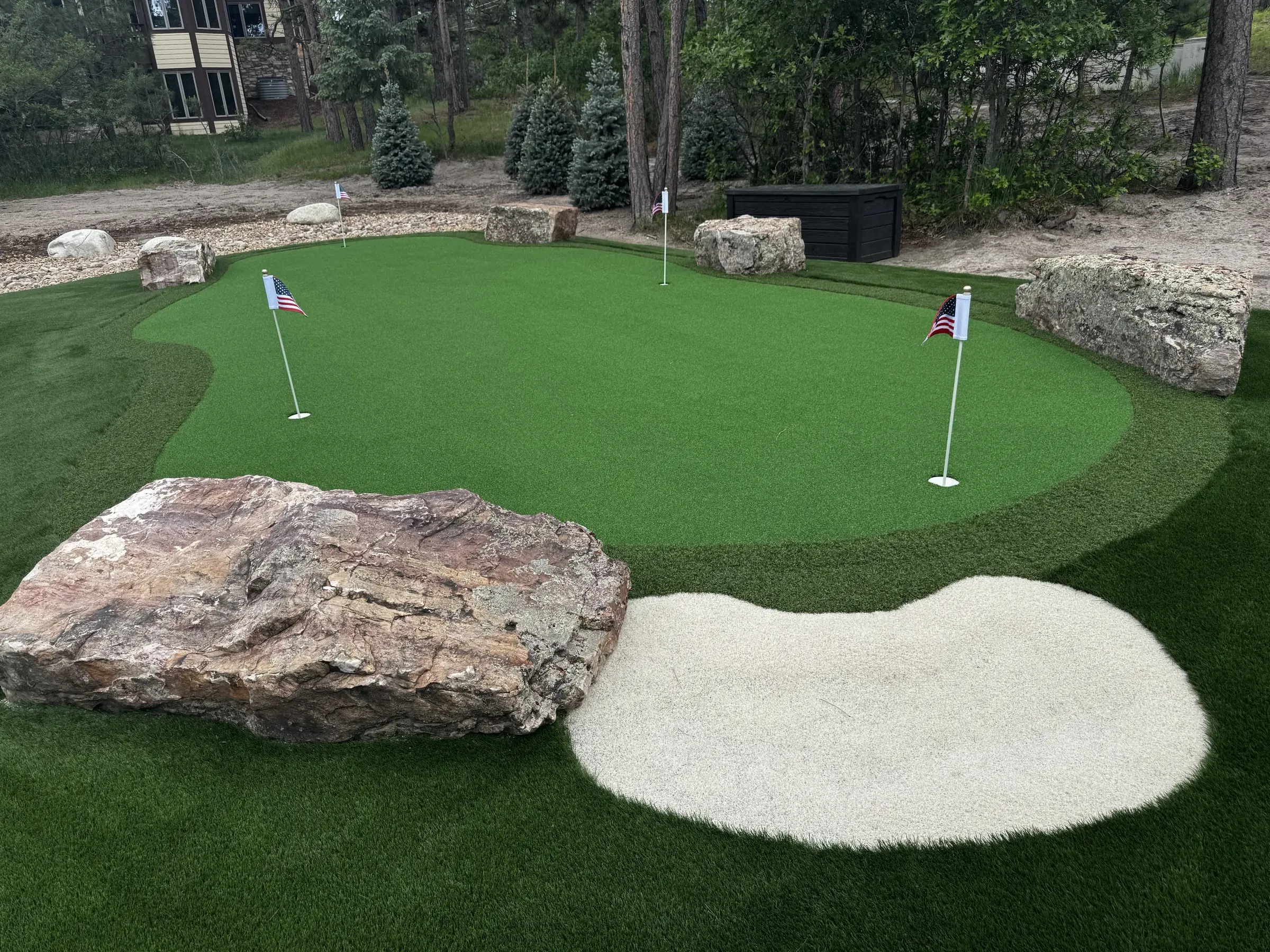 Close-up of a backyard putting green with boulder accents and a synthetic sand bunker in Larkspur