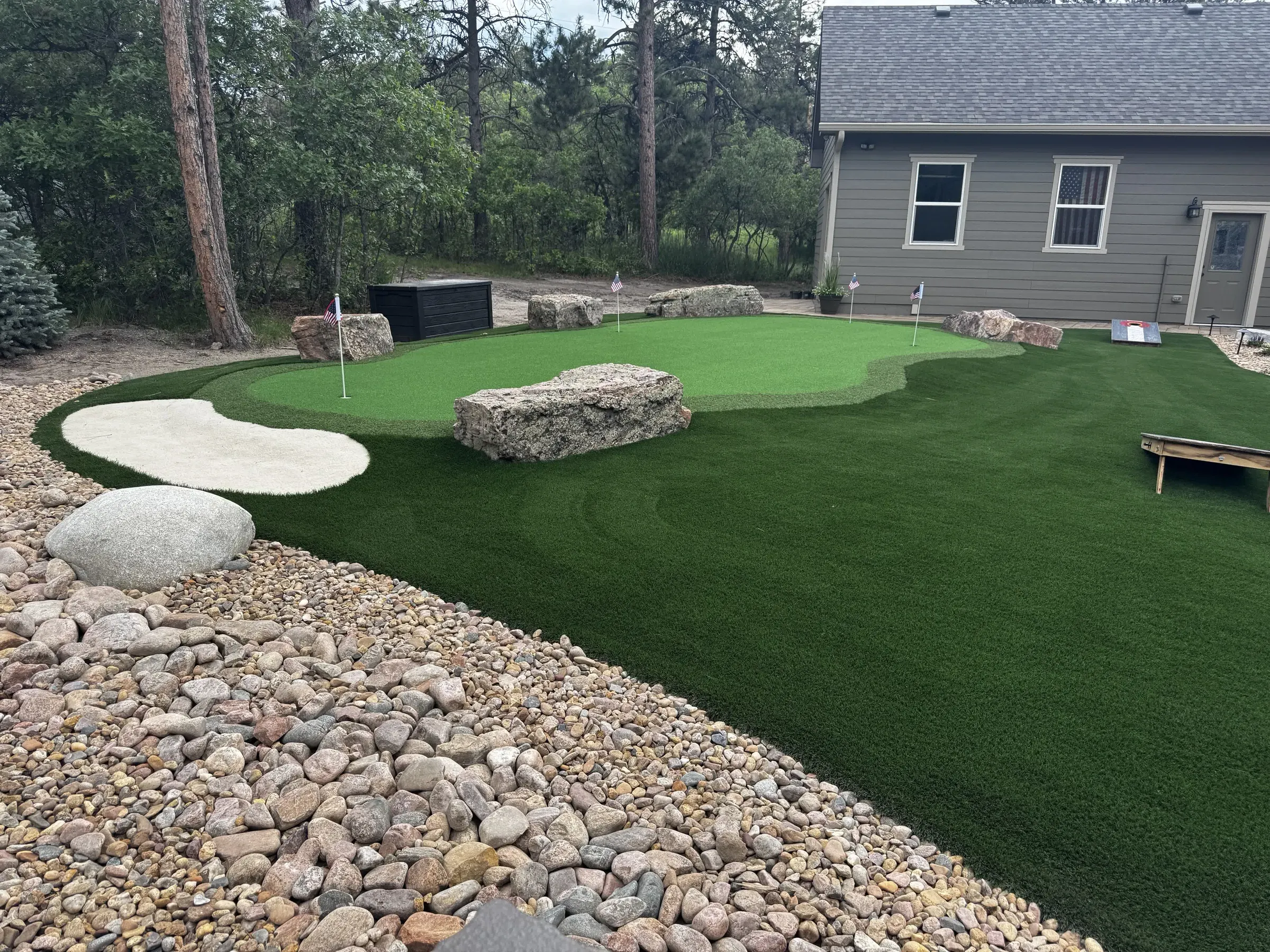 Artificial turf backyard with river rock borders, boulders, and a synthetic bunker in Larkspur