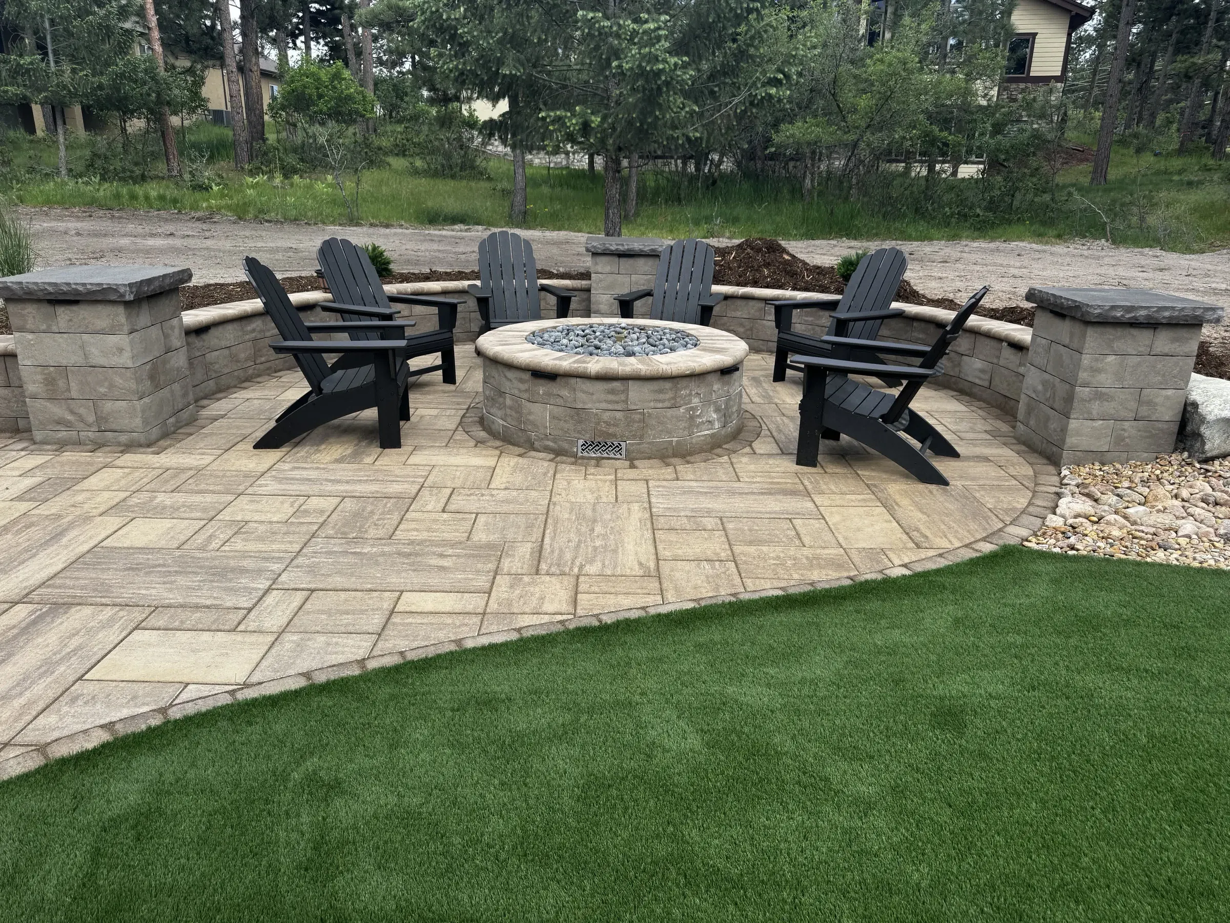 Paver patio with a round fire pit, curved seat wall, and Adirondack chairs in Larkspur