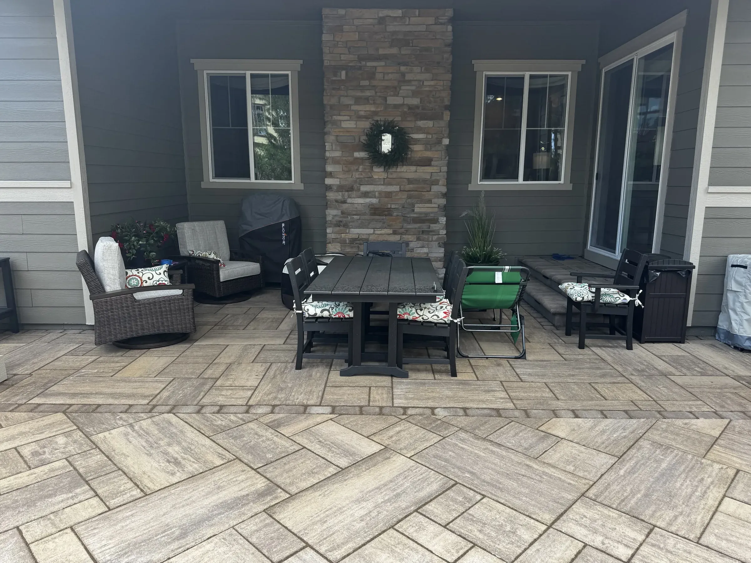 Paver patio dining and lounge area beside a stone fireplace accent wall in Larkspur