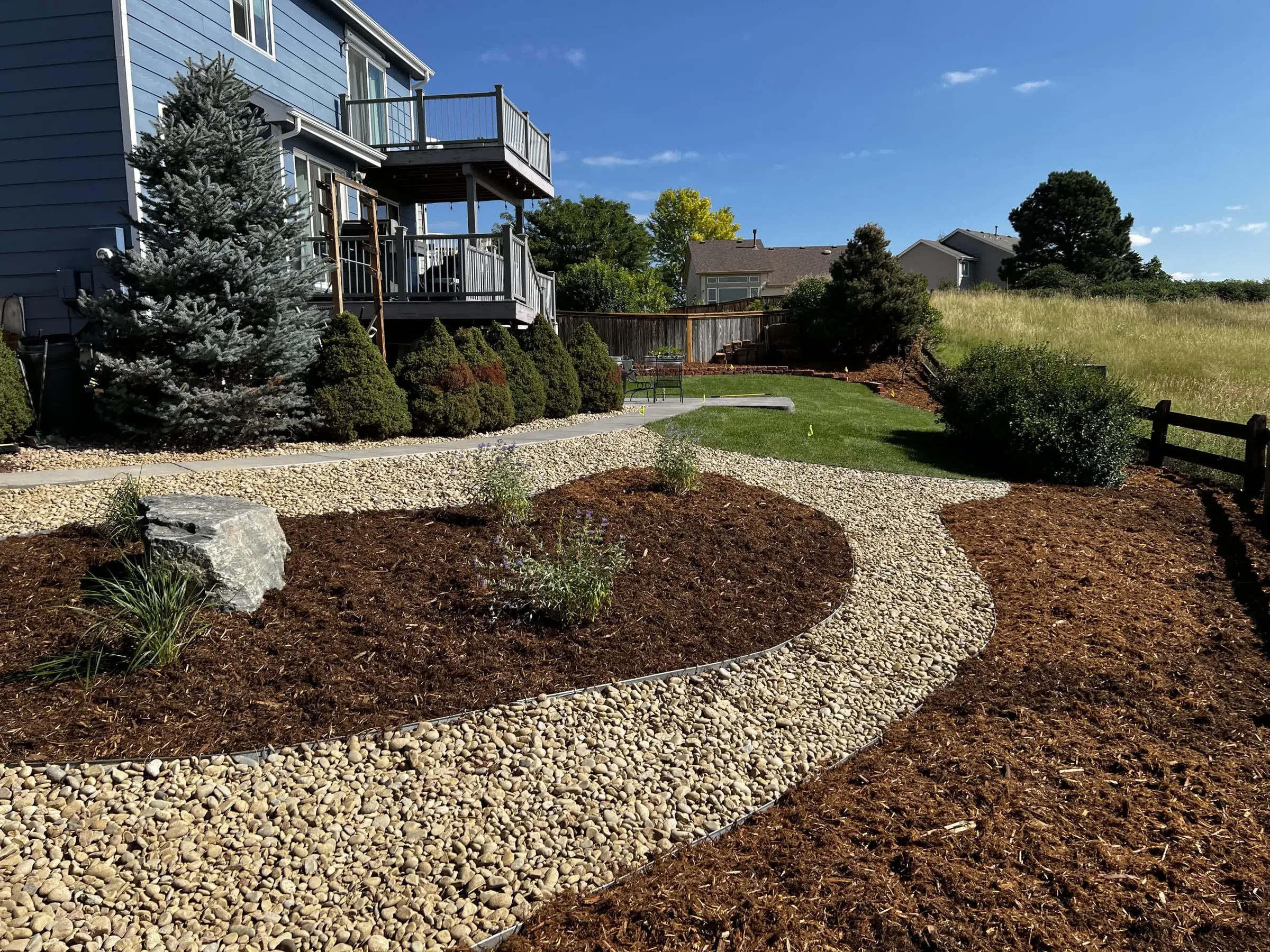 Backyard landscape renovation in Highlands Ranch with mulch planting beds, river rock borders, and new sod