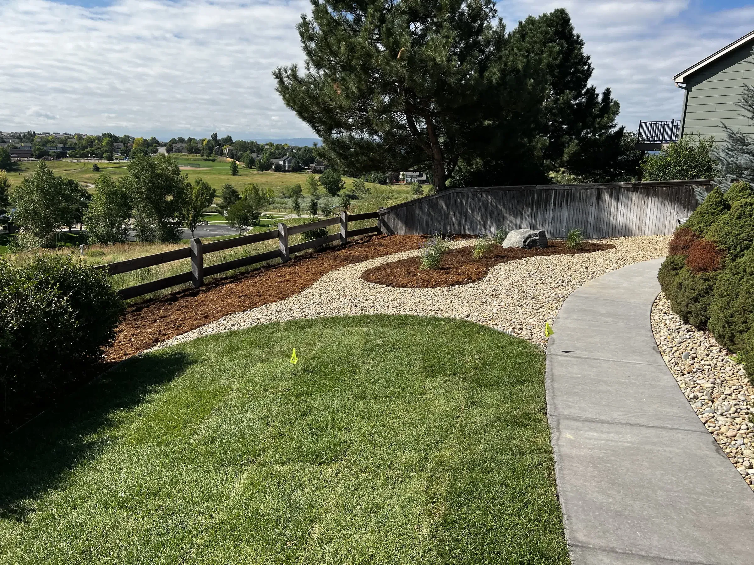 Curved concrete walkway with mulch beds and rock borders along a split-rail fence in Highlands Ranch