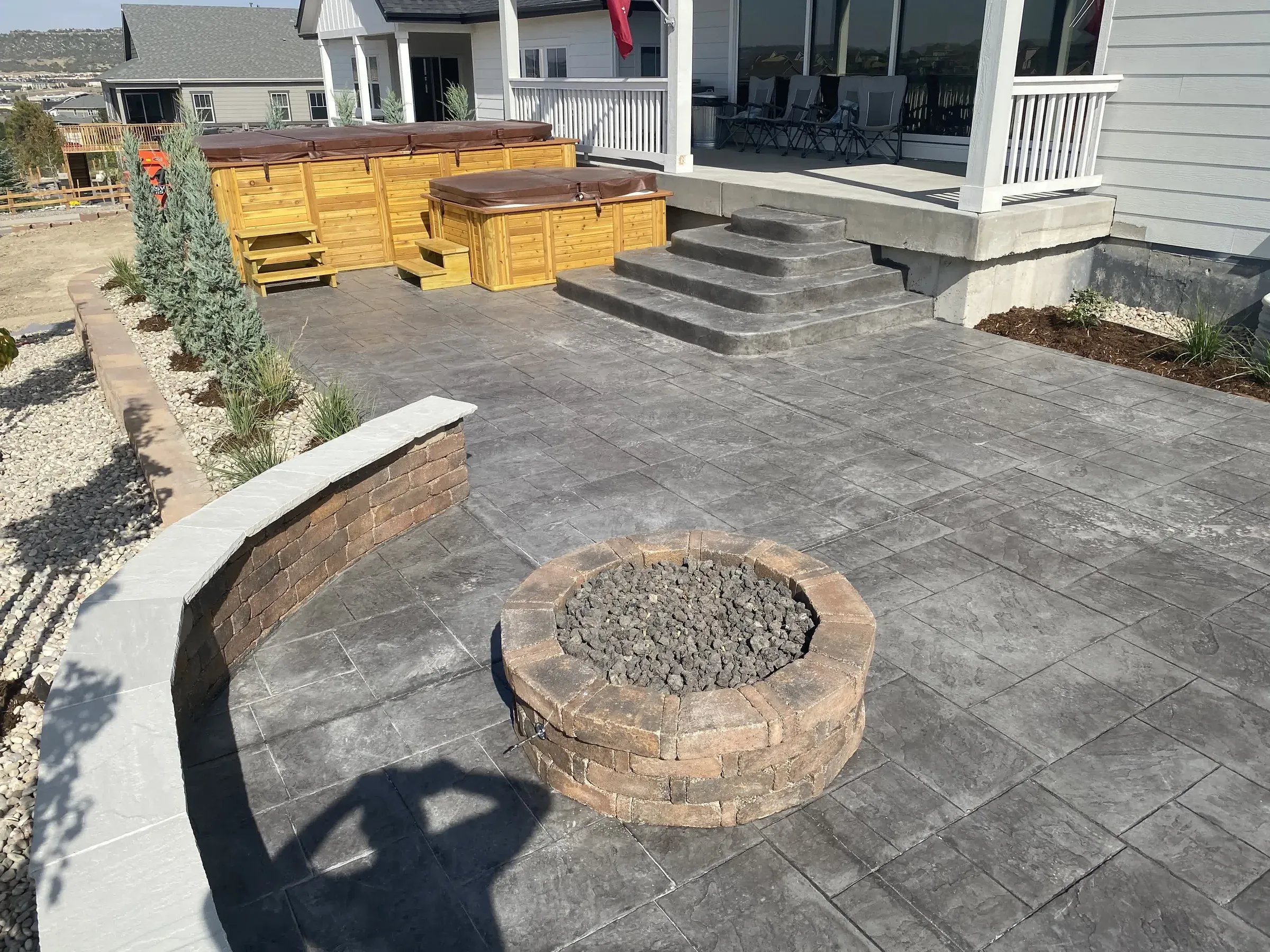 Stamped concrete patio, seat wall, and fire pit next to a built-in hot tub deck in Castle Rock
